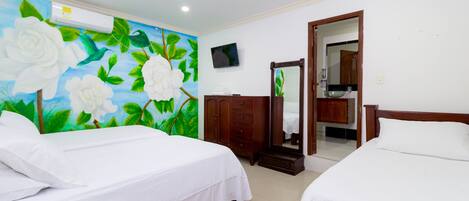 A hotel room with two beds, a large floral mural on the wall, a TV, and a wooden wardrobe.