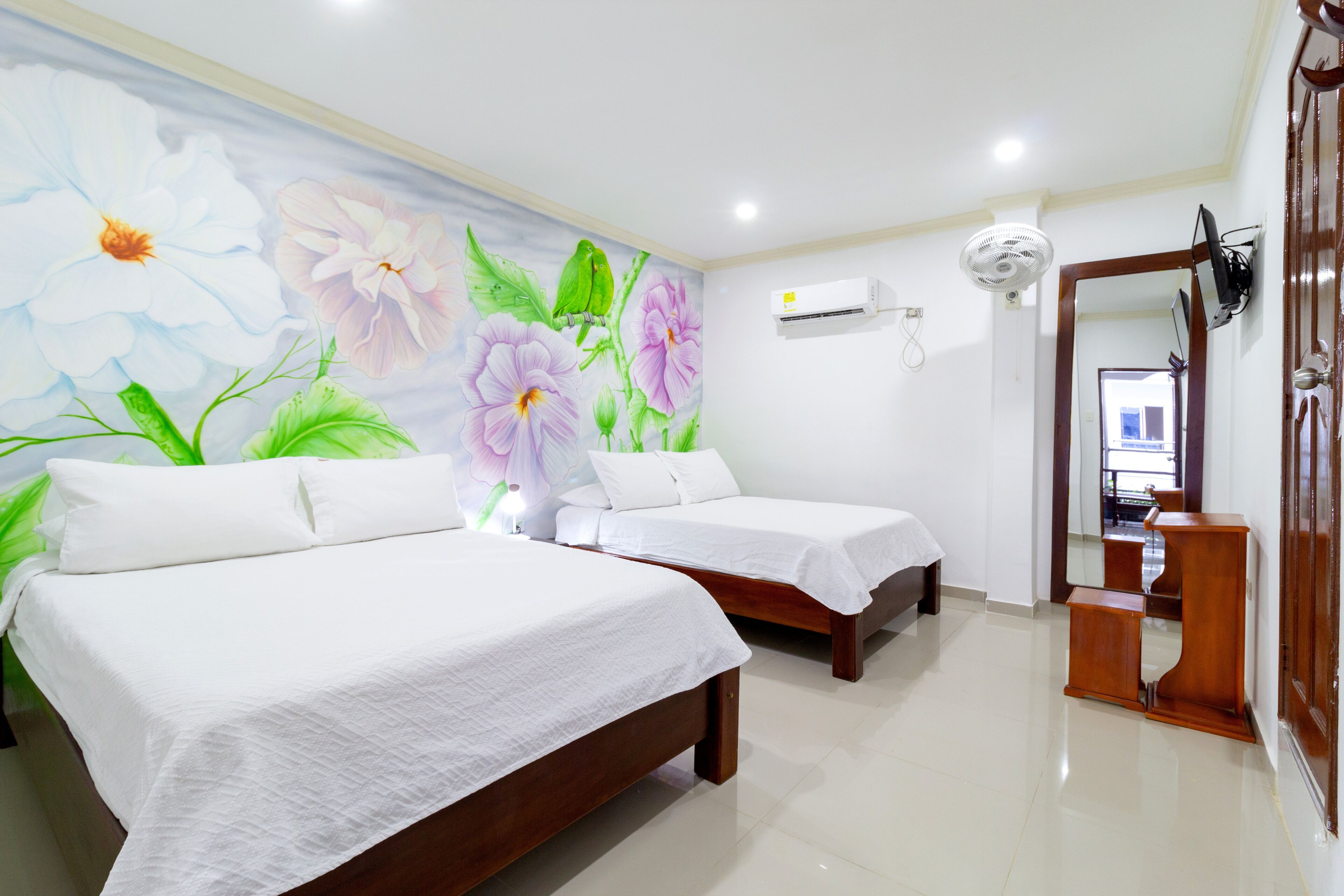 A hotel room with two beds, a mural of flowers on the wall, a ceiling fan, and a wooden cabinet.