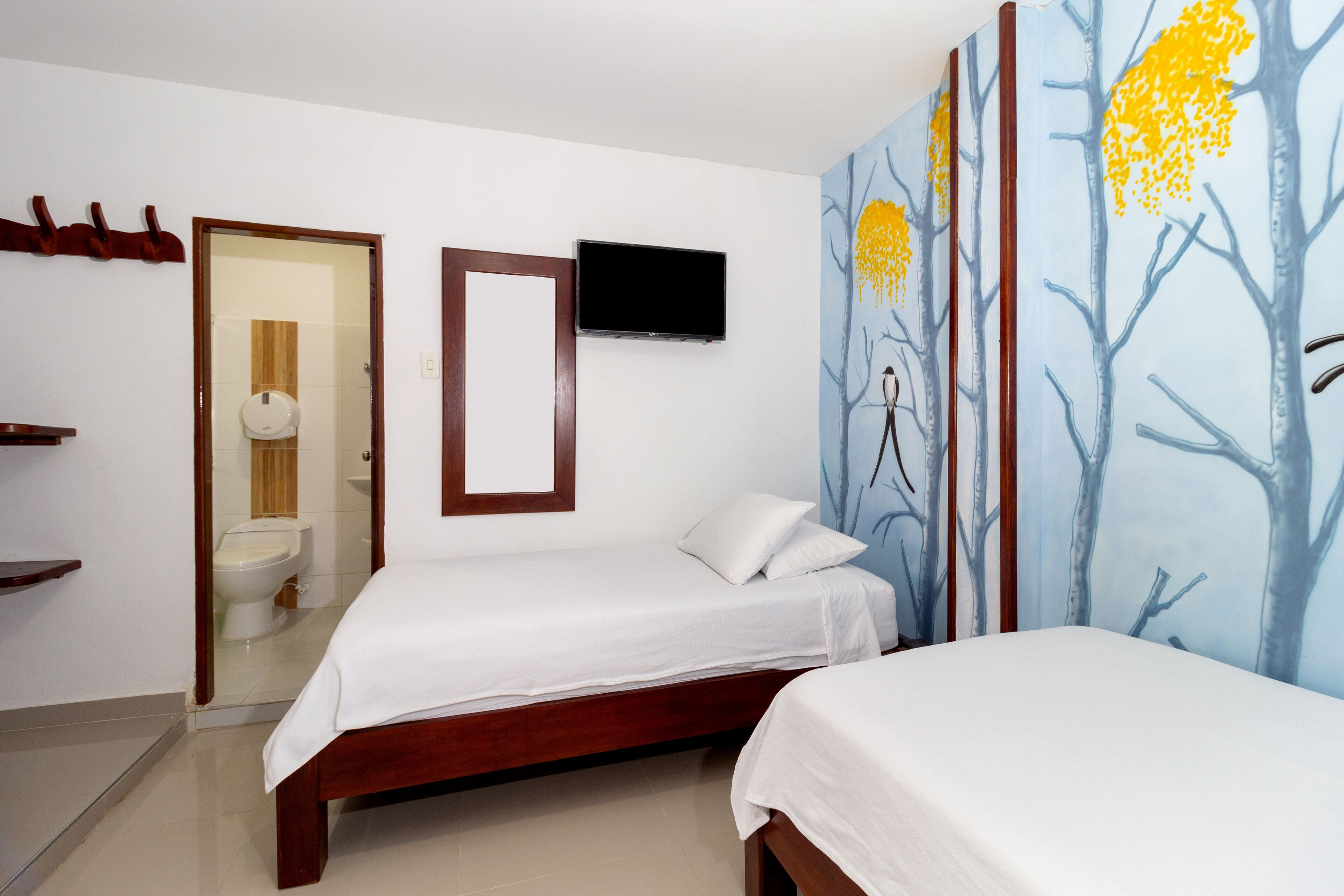 Quarto de hotel com duas camas, televisão, um quadro e banheiro visível por uma porta aberta.
