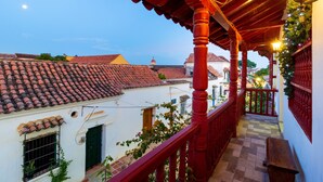 Un balcón con barandillas rojas, techo de tejas y vistas de edificios cercanos.