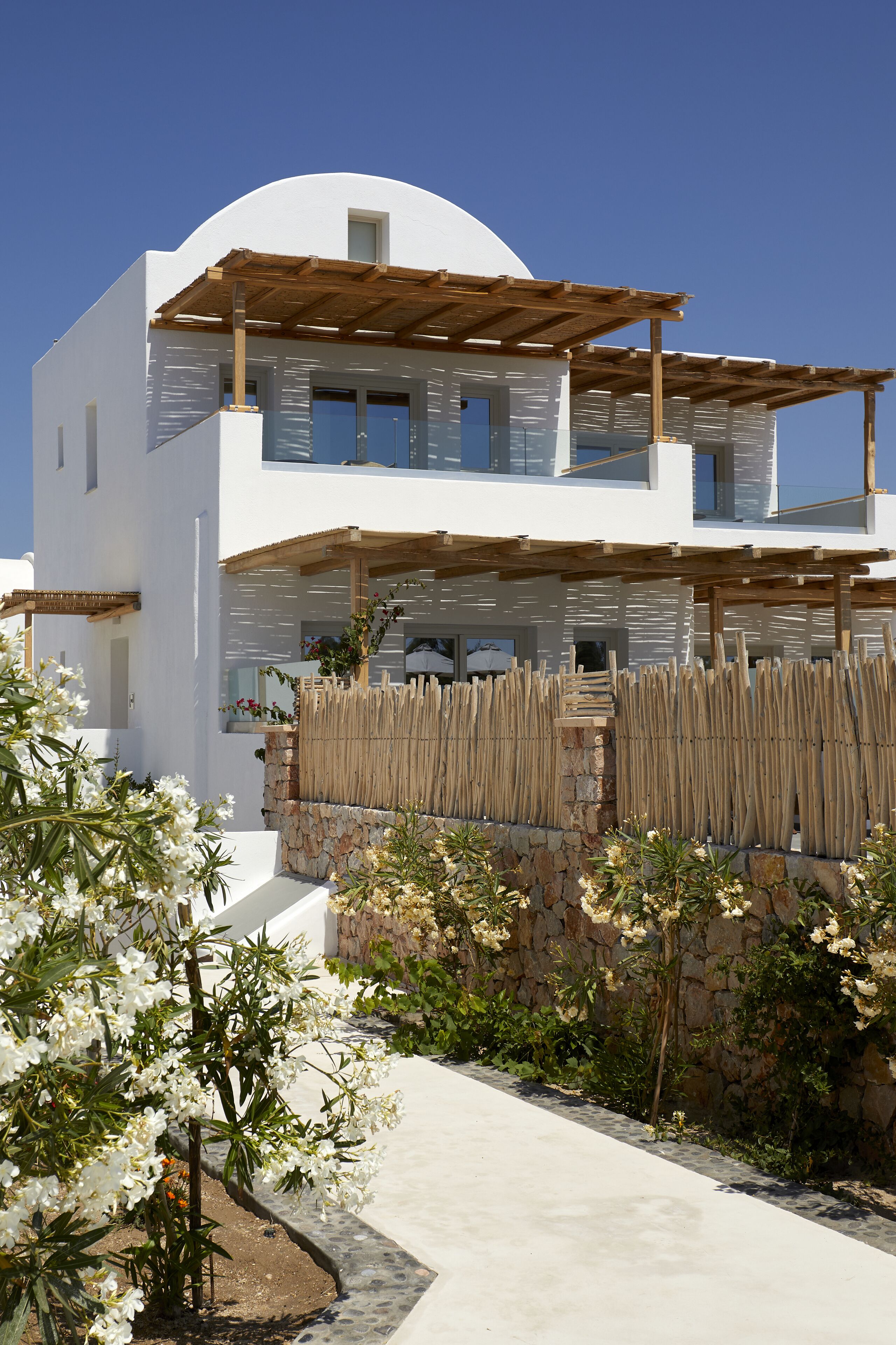 Una casa moderna de dos pisos con fachada blanca, una pérgola de madera y un muro de piedra con valla de madera.