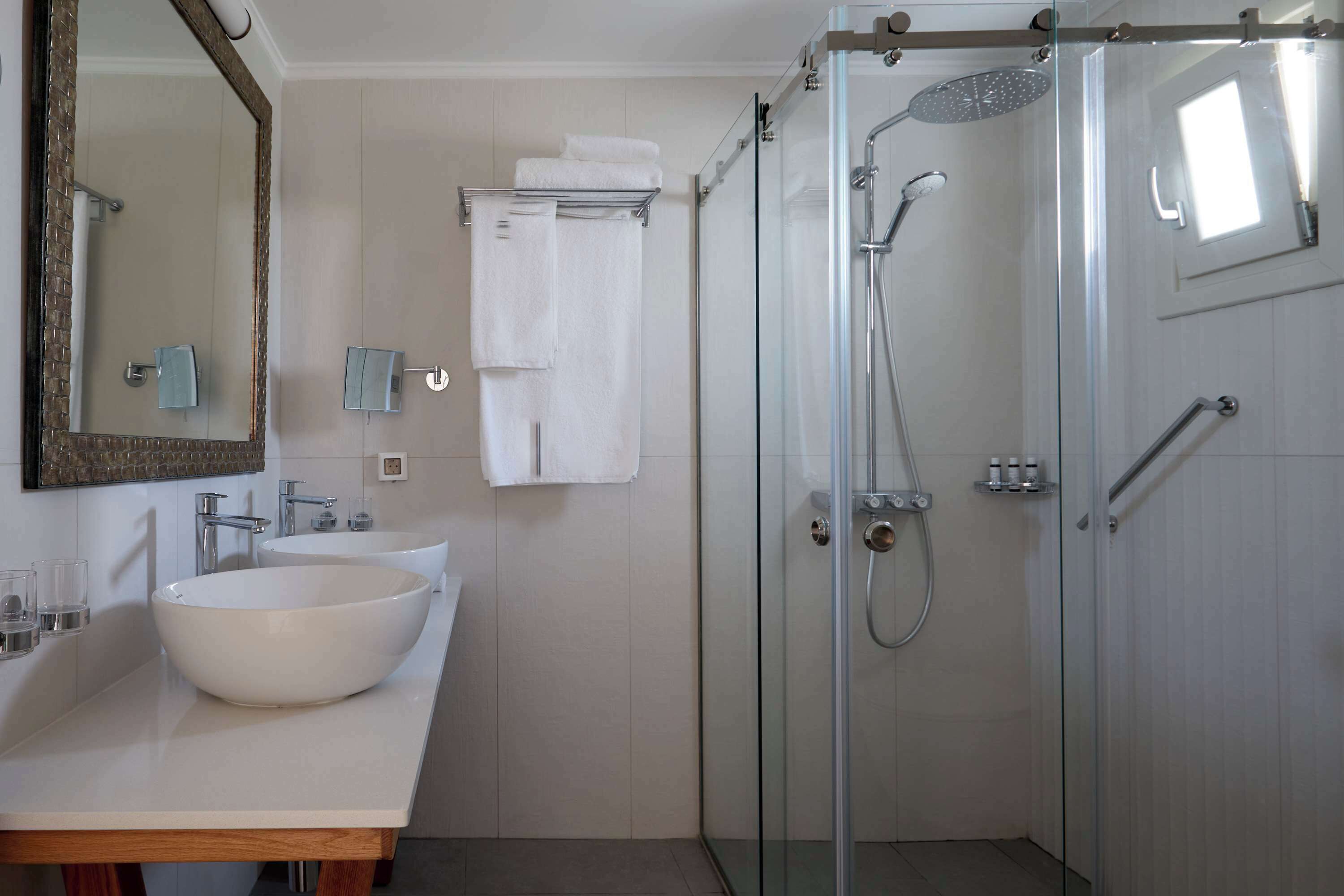 A modern bathroom with a large white sink, a glass-enclosed shower, and a mirror with a wooden frame.