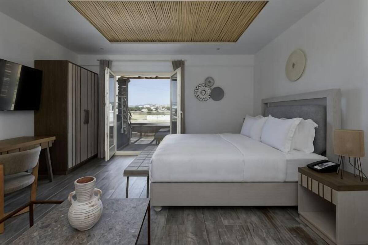 A modern bedroom with a bed, a desk, a TV, and a view of the outside.