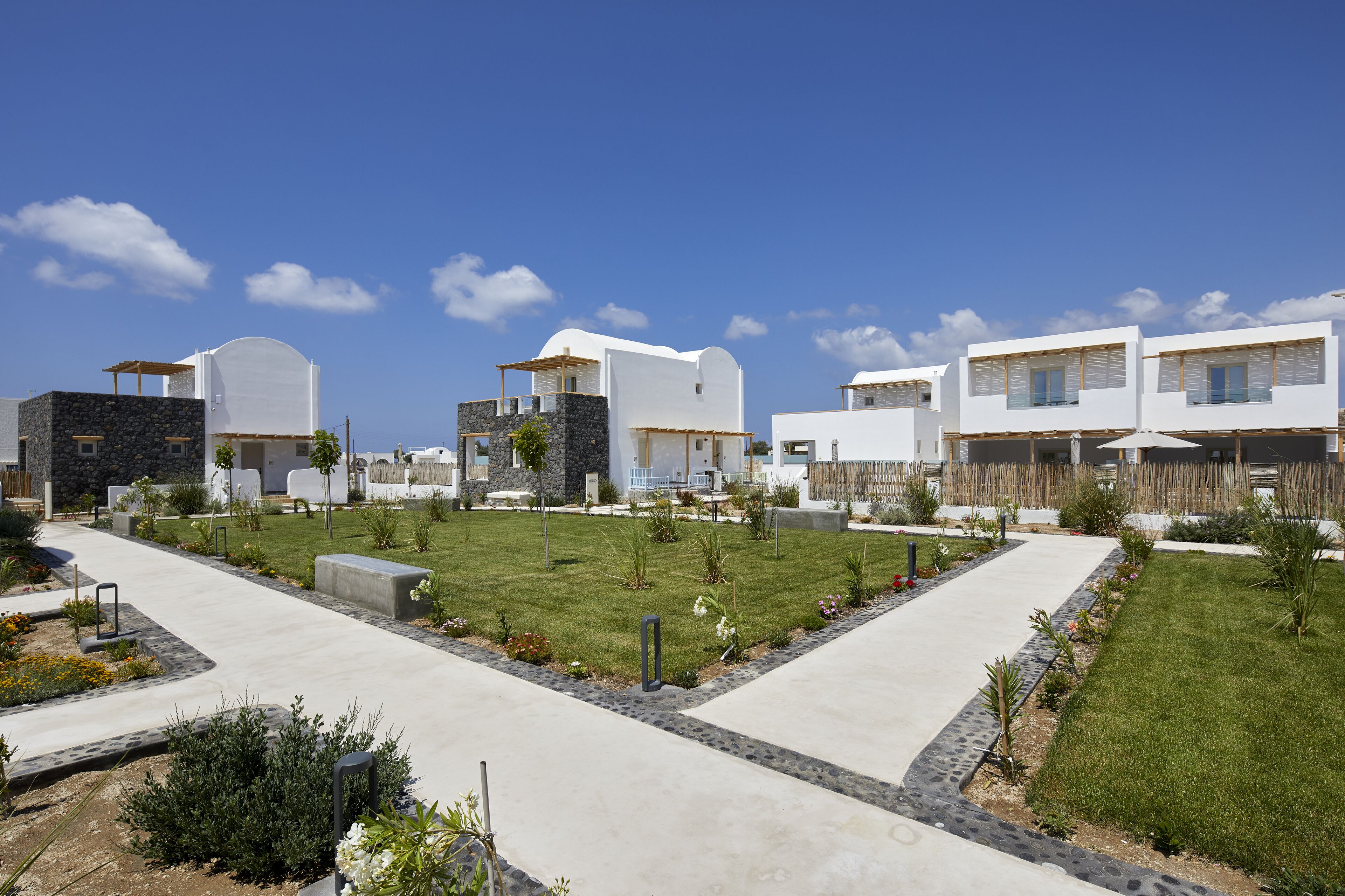 Un complejo residencial moderno con varios edificios de piedra y blanco, un área central cubierta de césped y un sendero pavimentado.