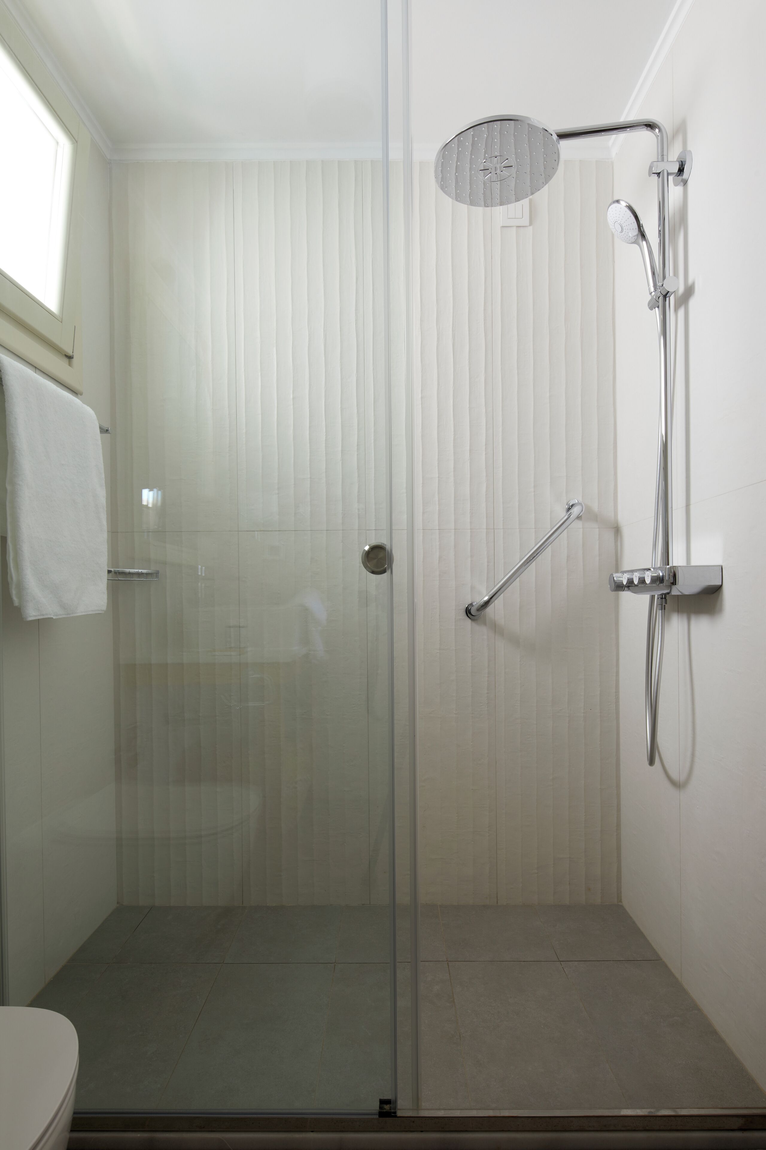 A glass-enclosed shower with a handheld showerhead and a handheld faucet.
