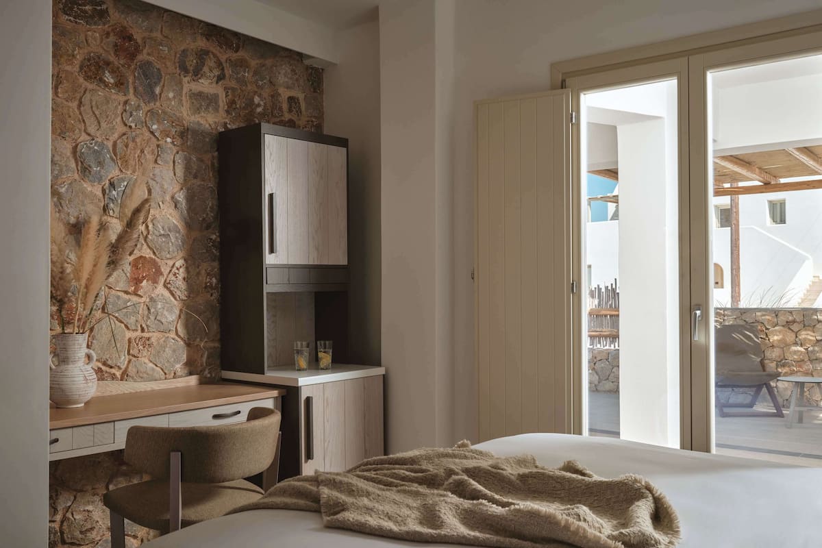 Une chambre avec un mur en pierre, un bureau en bois, un lit avec une couverture et une vue sur l’extérieur.