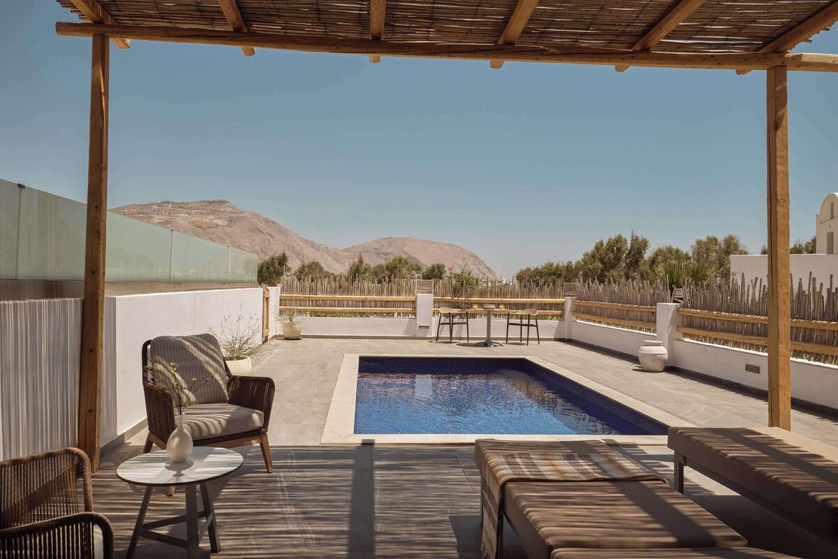 Un espace piscine aménagé sur le toit, avec une pergola en bois, des chaises longues et une vue sur les montagnes.