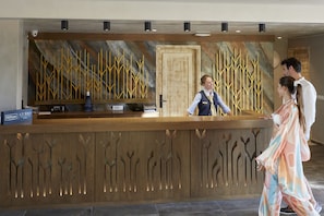 Ein Hotelrezeptionstresen mit Holzdesign und einem großen Wandbild abstrakter, gelber Linien.