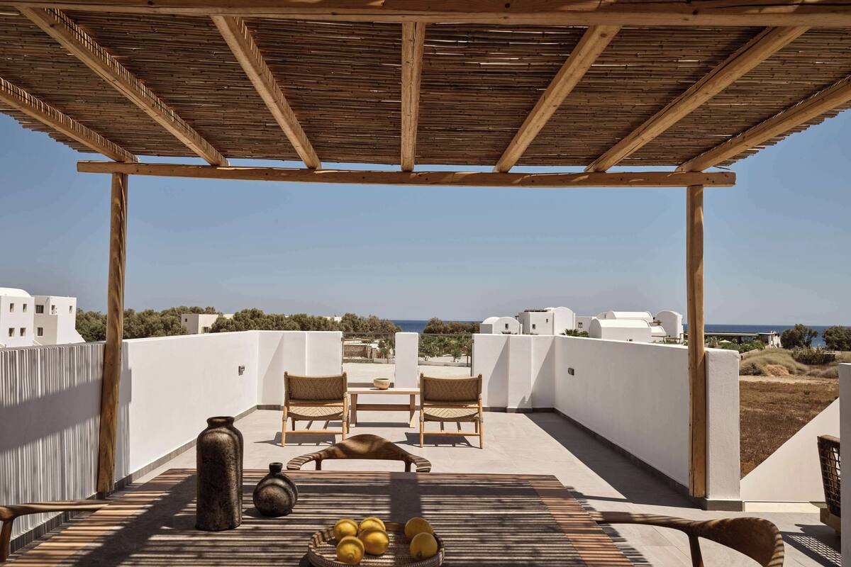 Un espace extérieur abrité, aménagé avec des sièges, offrant une vue sur la mer, et comprenant une table sur laquelle se trouve un saladier rempli de citrons, ainsi que deux chaises en osier.