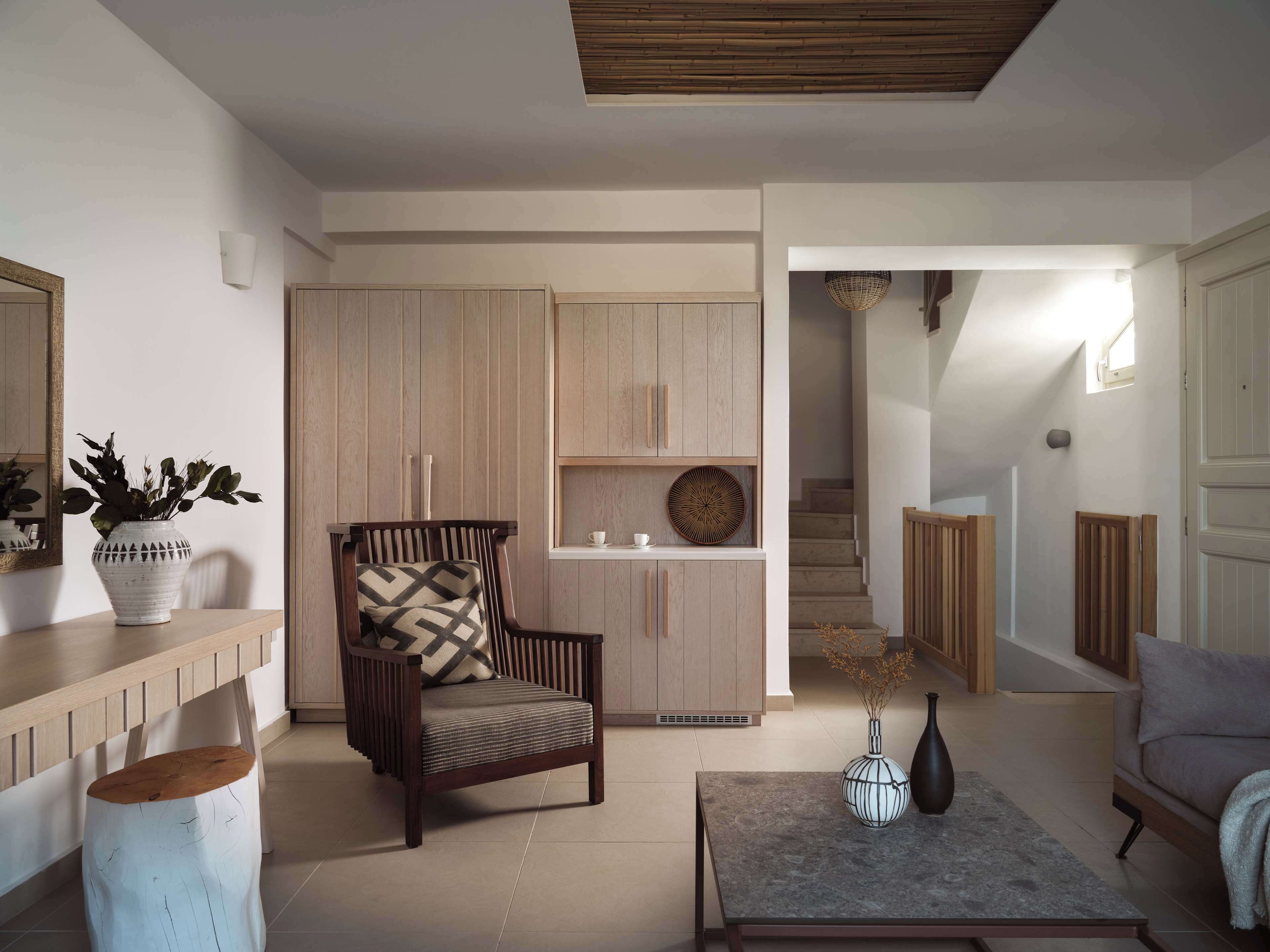 Un salon moderne avec un fauteuil en bois, une table basse et un coin repas doté de meubles de rangement en bois clair.