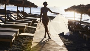 Een promenade langs het strand met ligbedden en rieten parasols.