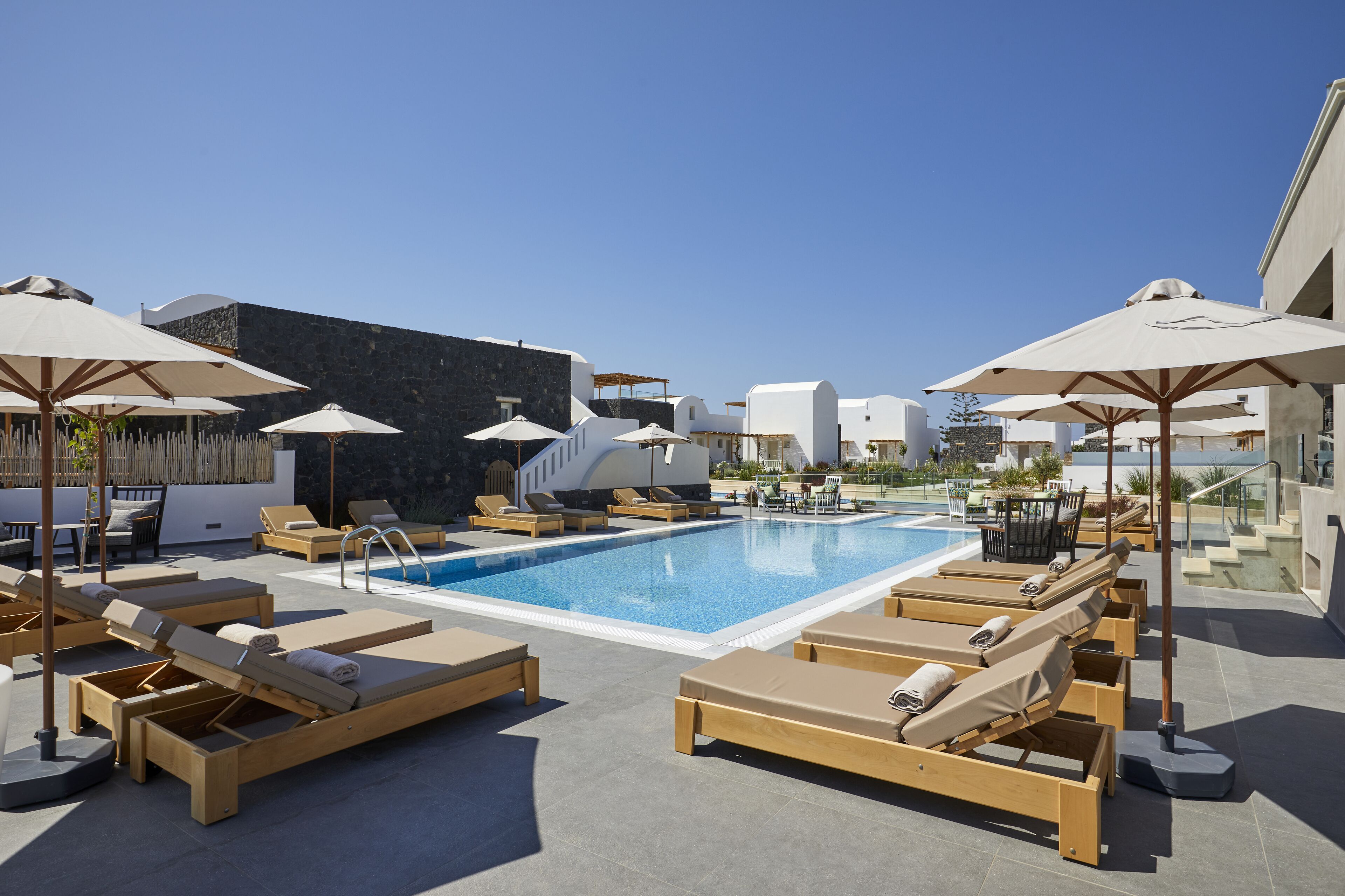 A rooftop pool area with sun loungers and umbrellas, surrounded by modern architecture.