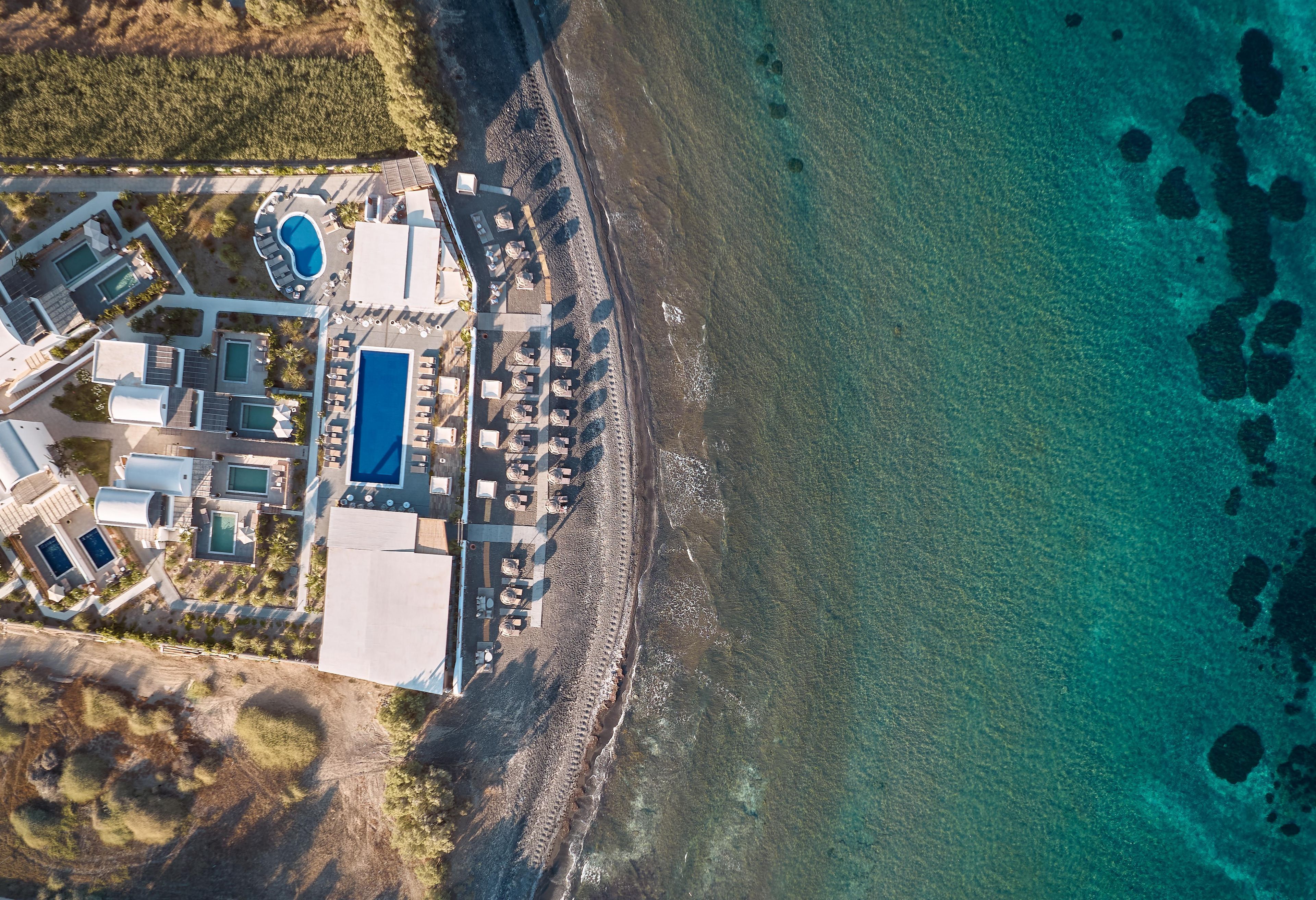 Vista aérea de un complejo turístico costero con varias piscinas, tumbonas y un litoral rocoso.