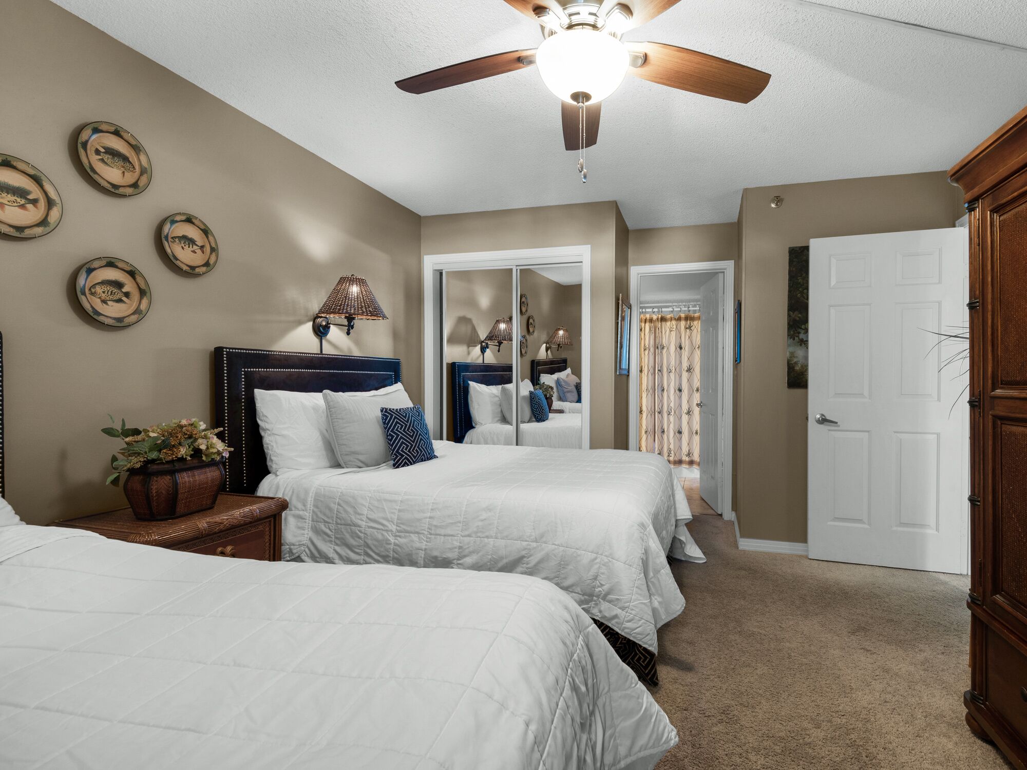 A bedroom with two beds, a ceiling fan, and a door leading to another room.