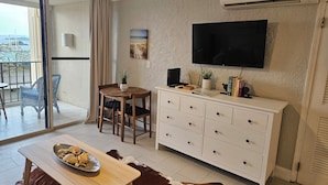 Ett modernt vardagsrum med en matplats, en platt-TV som är monterad på väggen, en takfläkt och utsikt över utomhusmiljön genom en skjutdörr i glas.