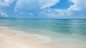 A beach with clear turquoise water and a sandy shore under a partly cloudy sky.