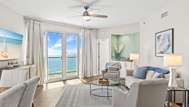 A spacious living room with a large window, a ceiling fan, and a view of the ocean.