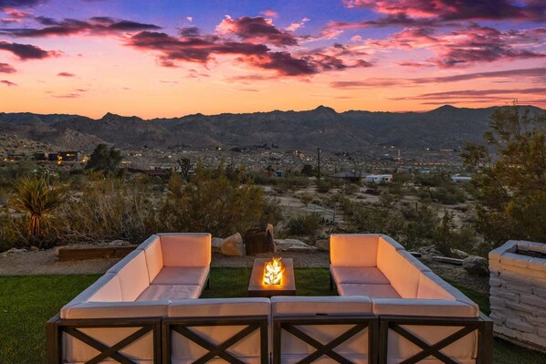 Une vue sur le coucher de soleil depuis une terrasse agrémentée d’un foyer extérieur, d’un espace salon et offrant un panorama sur le paysage désertique.