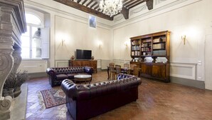 Un salon spacieux avec des canapés en cuir, un lustre, une cheminée et une bibliothèque.