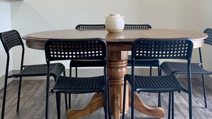 A round wooden table with a white pot in the center, surrounded by four black perforated chairs. Two abstract art pieces are hung on the wall above the table.