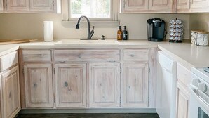 A kitchen with light wooden cabinets, a window above the sink, a coffee maker, and a patterned rug on the floor.