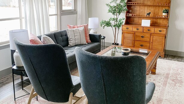 A modern living room with two dark armchairs, a wooden coffee table, and a cabinet with shelves.