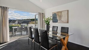 A modern dining area with a glass table and black chairs, a large abstract painting on the wall, and a view of mountains through the glass door.
