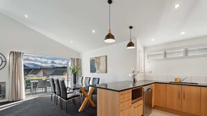 A modern kitchen with wooden cabinets, a black countertop, and a dining area with a glass table and chairs.