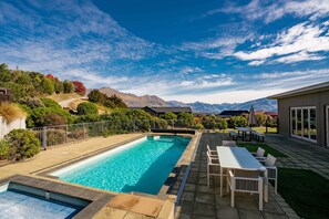 A swimming pool with a view of mountains, a patio with outdoor furniture, and a fenced garden area. - Treble Cone Views  - 3 Bedroom Apartment (Wanaka)