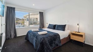 A modern hotel room with a large bed, a bedside table with a lamp, and a view of the city through the window.
