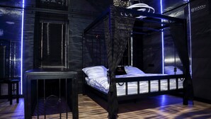 A modern bedroom with a four-poster bed, a small table, and a wall-mounted shelf. - Apartament BDSM Luxxx Częstochowa (Czestochowa)