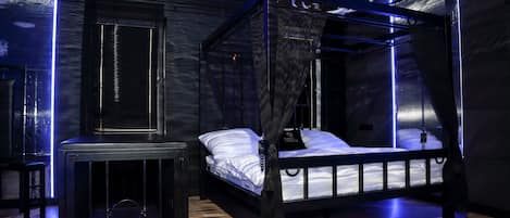 Een moderne slaapkamer met een hemelbed, een klein tafeltje en een wandplank.