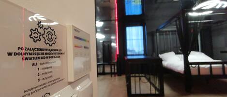 A hotel room with a bed, a bedside table, and a wall-mounted control panel.