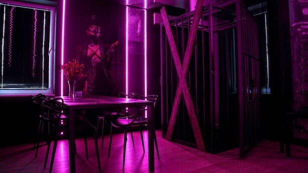 A modern dining area with a table and chairs, illuminated by purple ambient lighting. - Apartament BDSM Luxxx Częstochowa (Czestochowa)