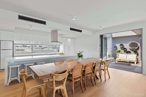 A modern kitchen with a large island, white cabinetry, and a dining area with wooden furniture.