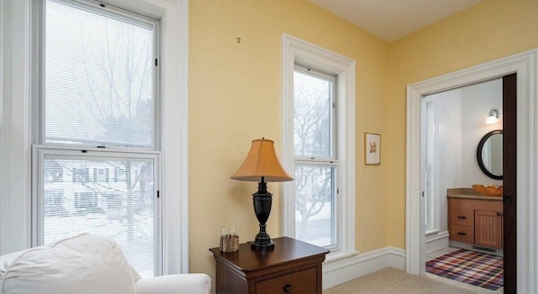 A room with two windows, a lamp on a nightstand, a door leading to a bathroom, and a small rug on the floor. - Haven on Howard - large home, great location (Grand Haven)
