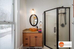 A bathroom with a wooden vanity, a glass shower enclosure, and a mirror with a light above it.