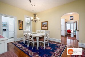 A dining area with a white table and chairs, a chandelier, and a patterned rug.