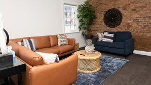 A living room with a brown leather sofa, a blue sofa, a round wicker coffee table, and a large potted plant. - McNamara Lane - CBD, 7 Smart TVs, Sleeps 11 (Orange)