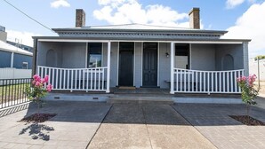 A single-story house with a front porch, two chimneys, and a small front yard with pink flowering plants. - McNamara Lane - CBD, 7 Smart TVs, Sleeps 11 (Orange)