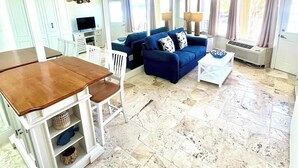 Un amplio salón con un sofá azul, una mesa de centro y una mesa de comedor con sillas.