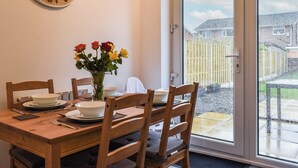 A dining area with a wooden table, chairs, a vase with flowers, and a wall clock. - 3 bedroom accommodation in St Annes (St Annes)
