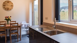 A modern kitchen with a large window, a built-in sink, and a wooden dining table with chairs. - 3 bedroom accommodation in St Annes (St Annes)