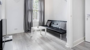 Una sala de estar moderna con un sofá de cuero negro, una mesa de centro blanca y cortinas grises.
