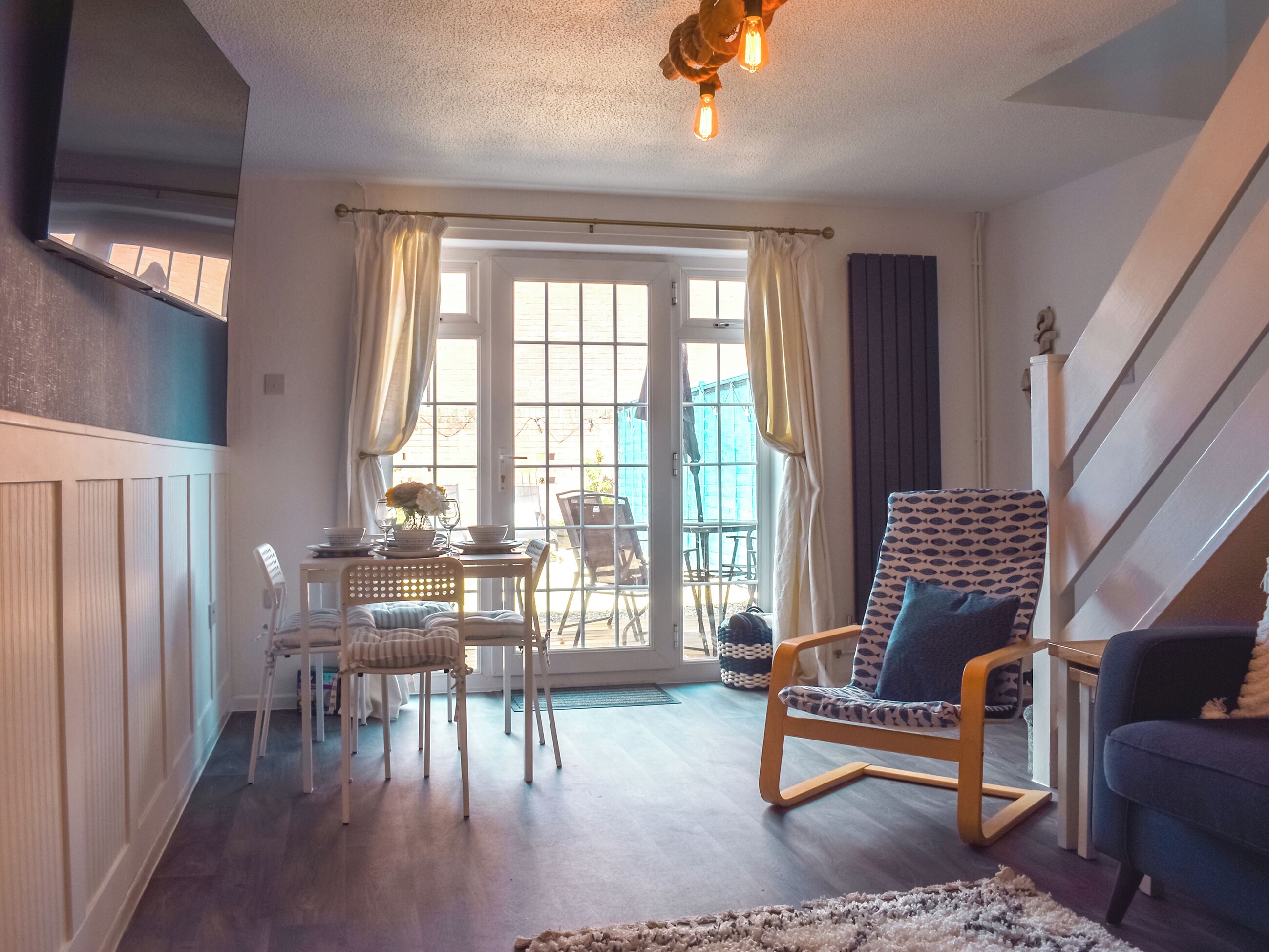 Un salon chaleureux avec un coin repas, un escalier et une vue à travers la porte vitrée.