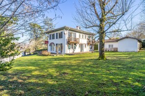 Traditional two-story home with a balcony and pitched roof, set amidst a well-manicured lawn.