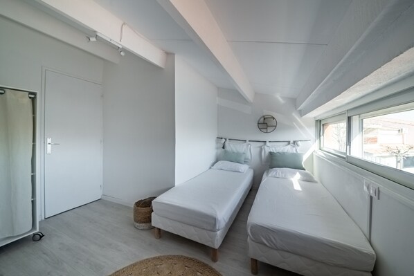 A modern bedroom with two single beds, a large window, and a white door.