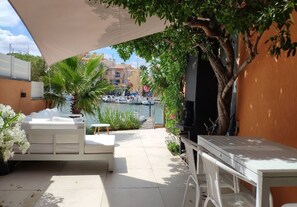 A patio with a white sofa, a dining table, and a view of a marina with boats.