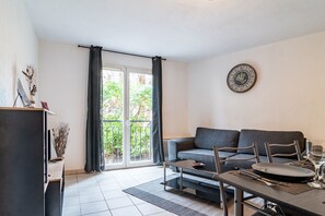 Uma sala de estar moderna com um sofá cinzento, uma mesa de jantar posta para dois e uma janela grande com cortinas.