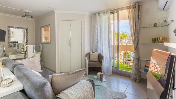A living room with a grey sofa, a glass coffee table, a white cabinet, and a sliding glass door leading to a balcony.